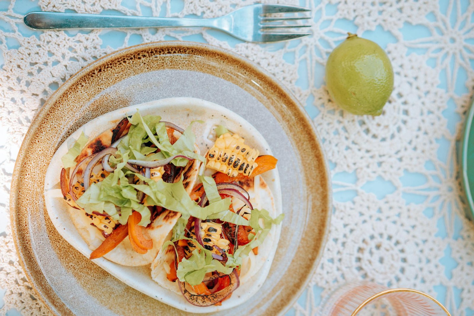 Colorful Mexican grilled vegetable tacos served on a decorated table with lime and intricate tablecloth.
