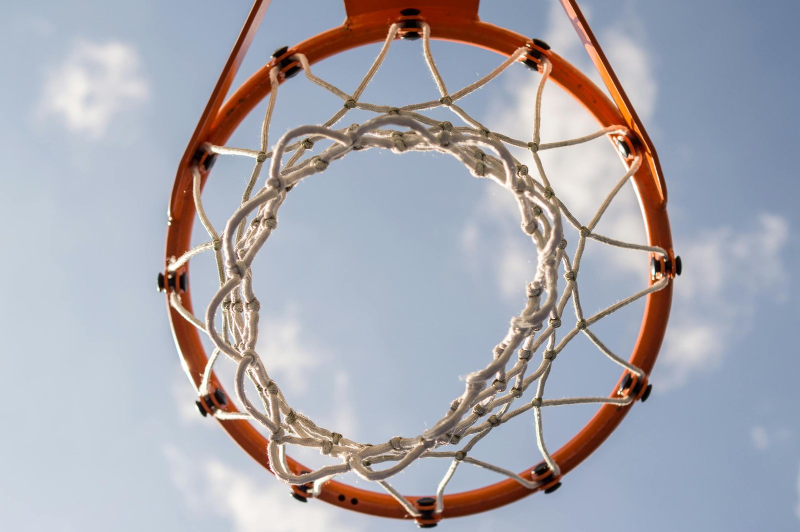 Close-up of a basketball hoop with net against a clear blue sky, ideal for sports themes.