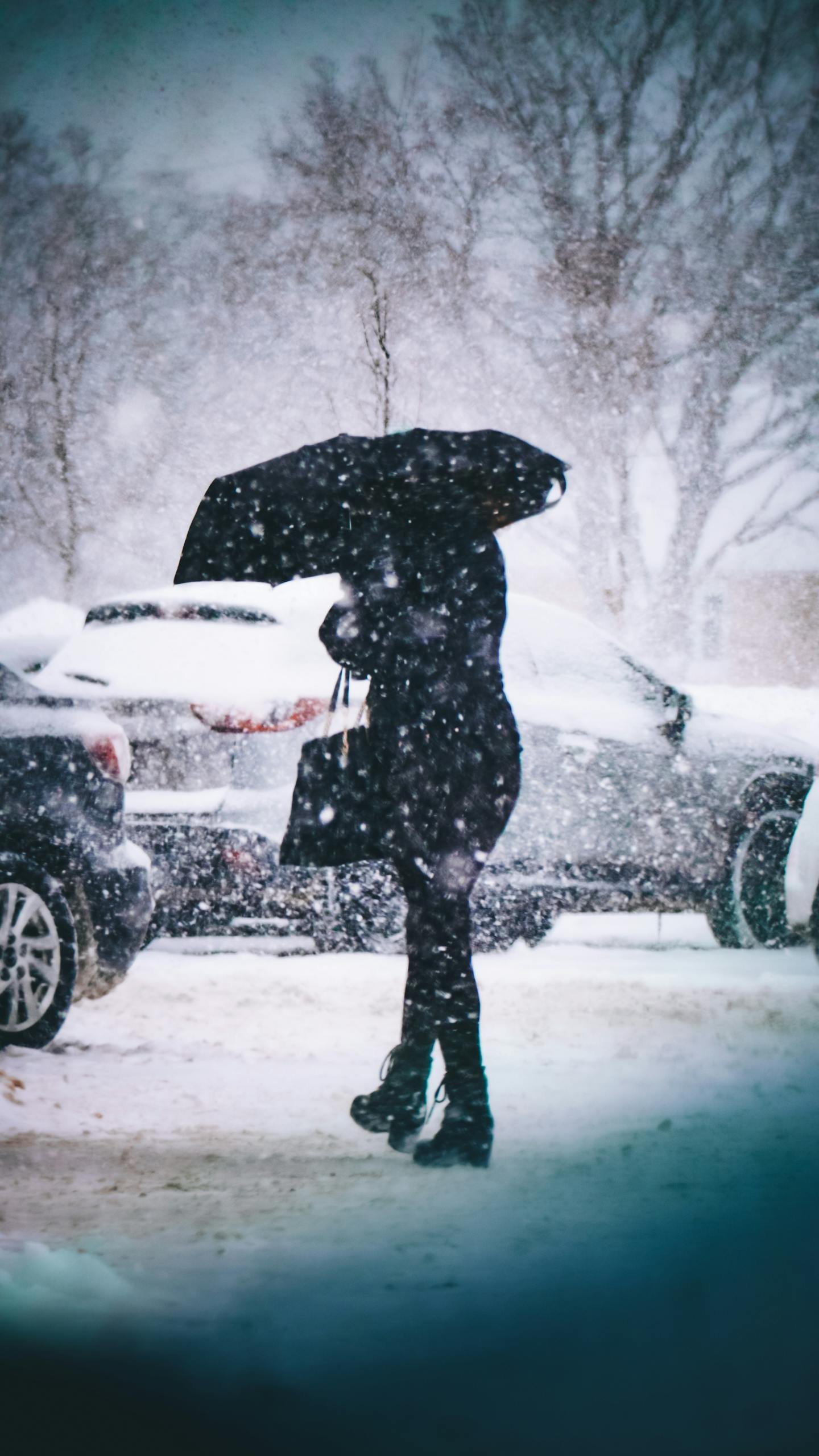 Silhouette of a woman in winter clothing walking through a snowy car park with an umbrella.