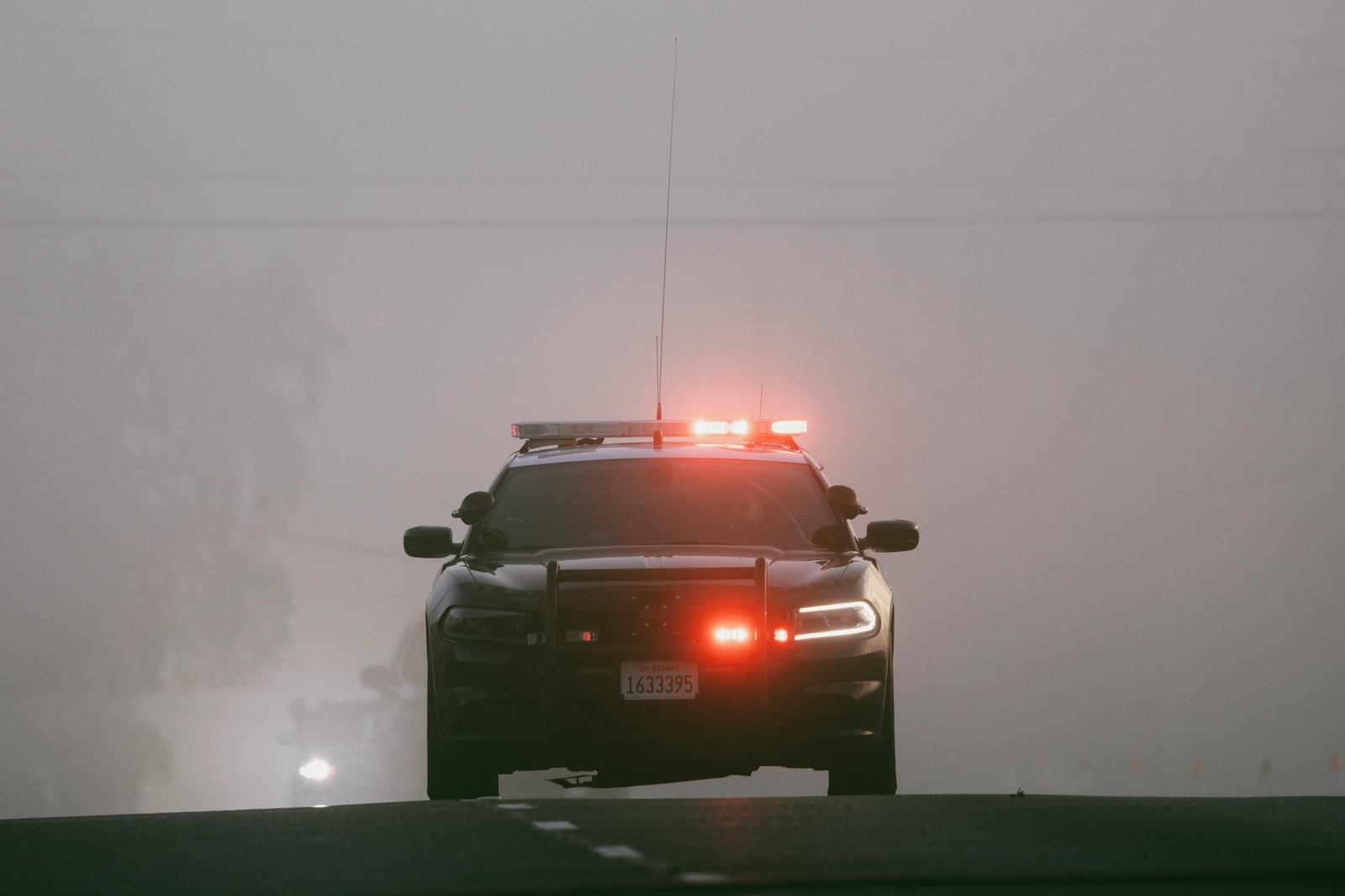 Red lights illuminate a foggy road as a police car approaches, creating an intense atmosphere.