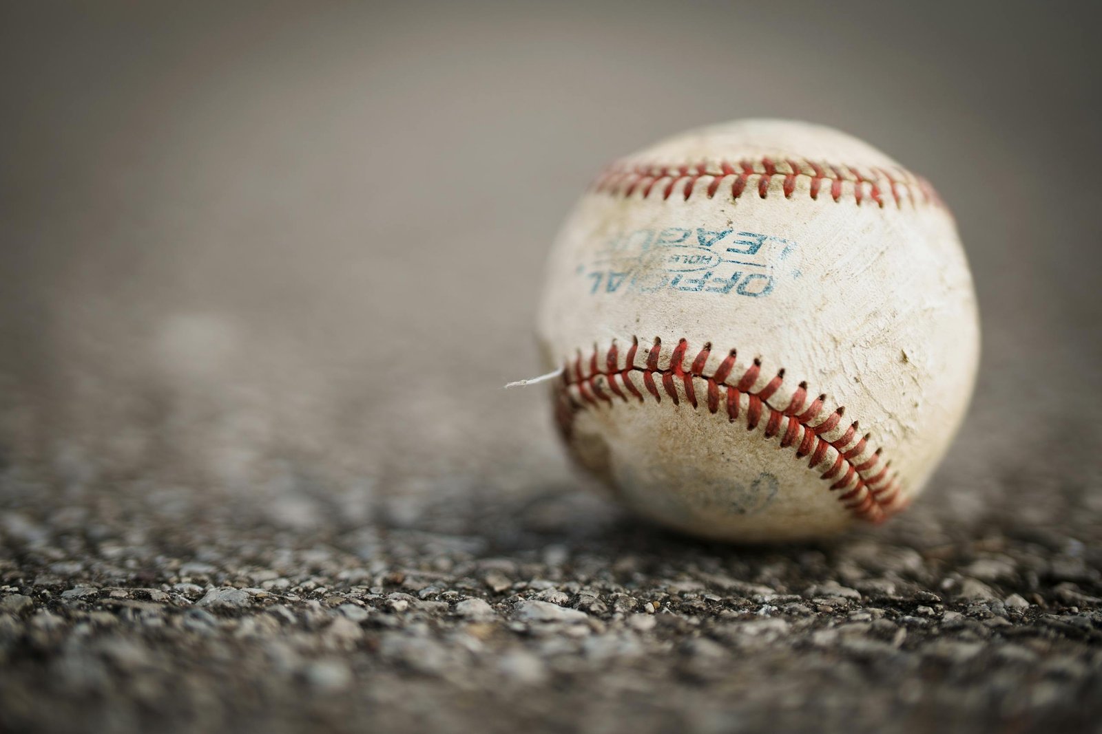 Detailed close-up of a worn baseball resting on a textured asphalt ground, emphasizing its use in sports.