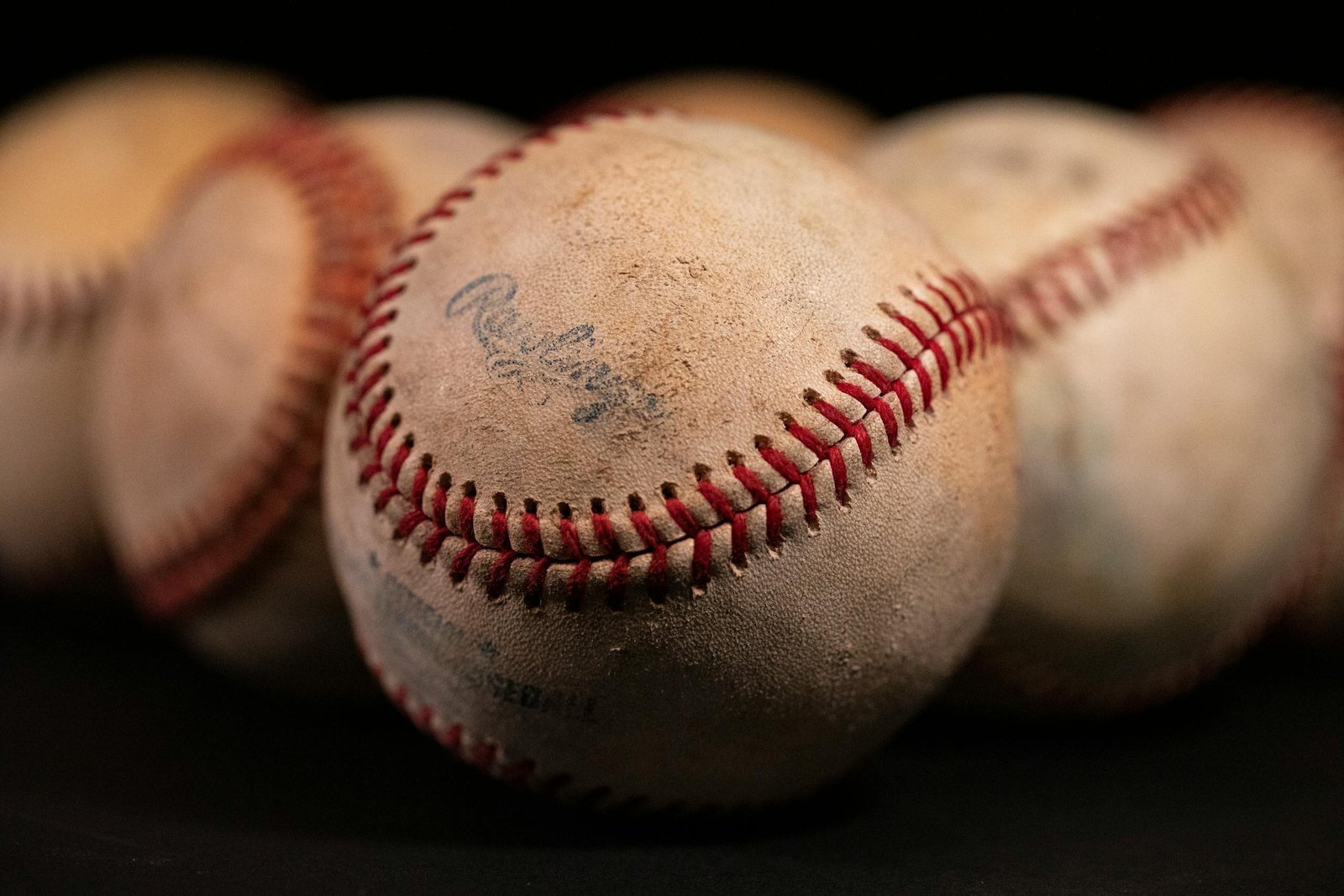 Focused close-up of old baseballs with visible stitching and texture against a dark background.