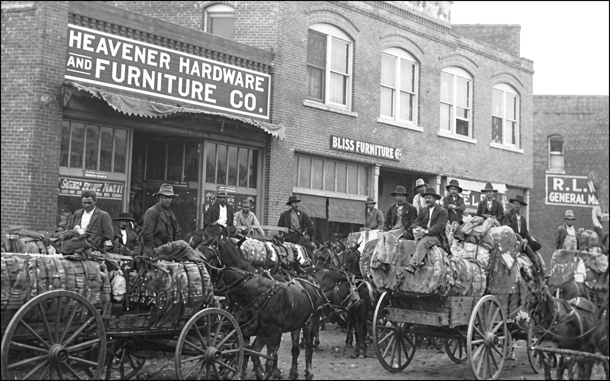 Historic photo of farmers hauling cotton through downtown Heavener, Oklahoma, after 1910, with the Bliss Building visible in the background